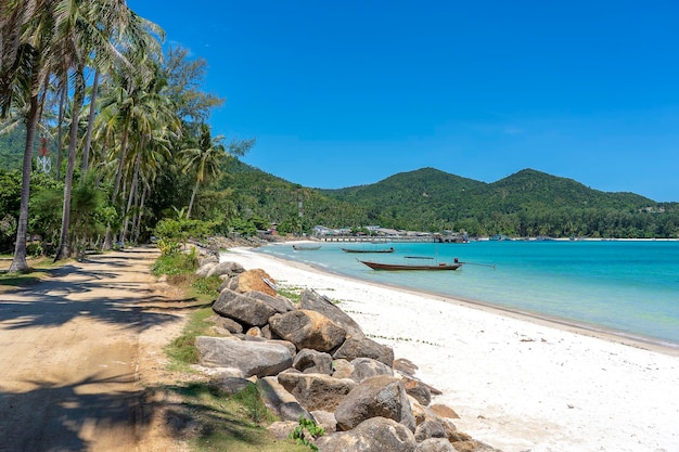 Beautiful bay with dirt road blue sea water coconut palm trees and boats Tropical sand beach and sea water on island Koh Phangan Thailand