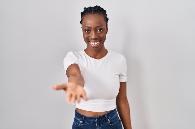 Beautiful black woman standing over isolated background smiling cheerful offering palm hand giving assistance and acceptance