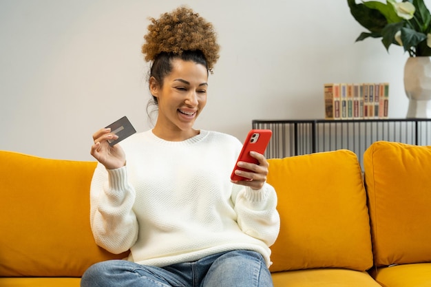 Beautiful black woman using a credit card for shopping and banking online with a mobile phone while