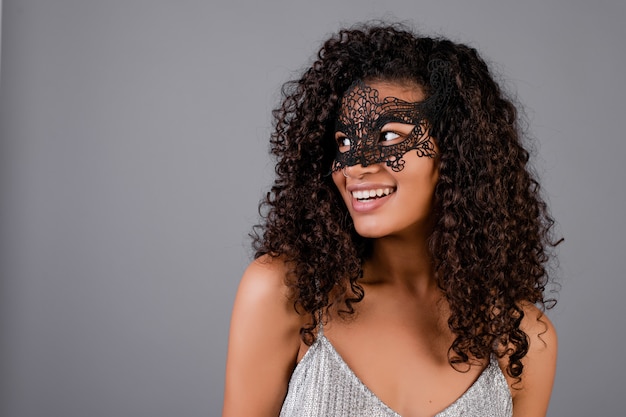 Beautiful black woman wearing elegant masquerade mask isolated over grey