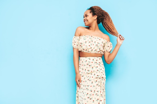 Beautiful black woman with afro curls hairstyle Smiling model dressed in summer dress Sexy carefree female posing near blue wall in studio Tanned and cheerful