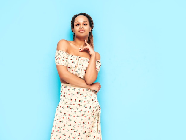 Beautiful black woman with afro curls hairstyle Smiling model dressed in summer dress Sexy carefree female posing near blue wall in studio Tanned and cheerful