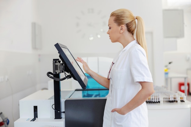 Beautiful blond laboratory assistant standing in lab and using computer to enter test results.