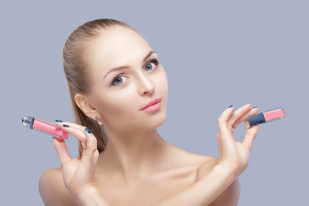 beautiful blond woman holding a pink lip gloss on a gray background. lip makeup