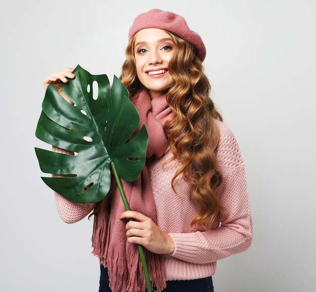 Beautiful blond woman with long wavy hair wearing casual smiling and holding a leaf of a large tropical flower