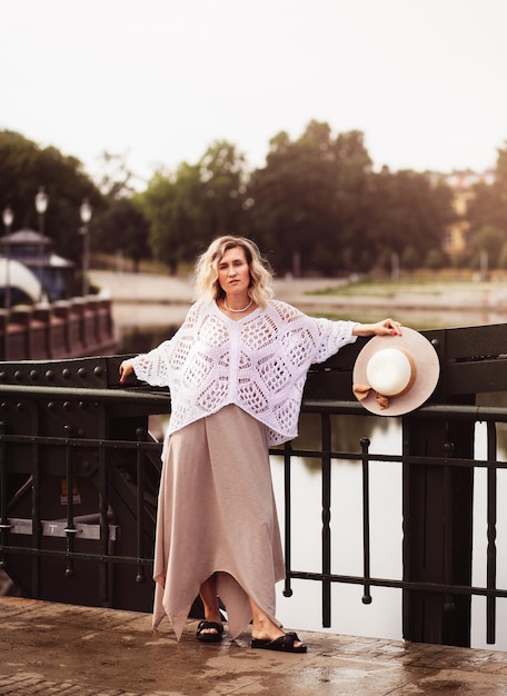 Beautiful blond young woman wearing dress and straw hat enjoying sunrise on seafront in old european town Fashion and style Summer travel