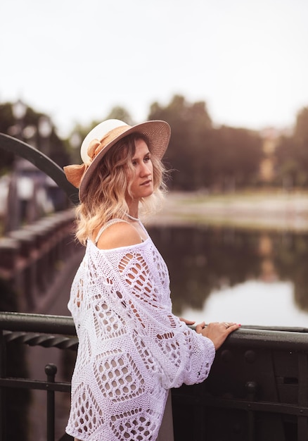 Beautiful blond young woman wearing dress and straw hat enjoying sunrise on seafront in old european town Fashion and style Summer travel