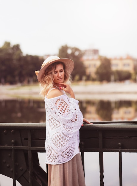 Beautiful blond young woman wearing dress and straw hat enjoying sunrise on seafront in old european town Fashion and style Summer travel