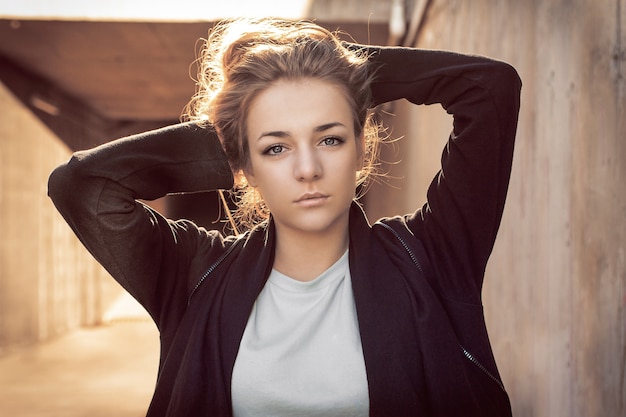 Beautiful blonde in a black cape posing against the background of a concrete wall