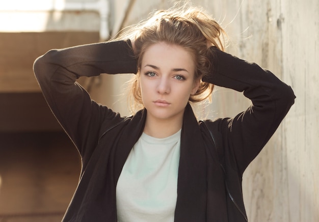 Beautiful blonde in a black cape posing against the a concrete wall