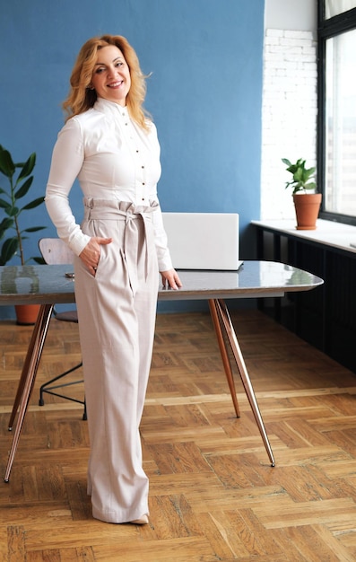 Beautiful blonde business woman in a blouse trousers and highheeled shoes smiles and looks at the camera