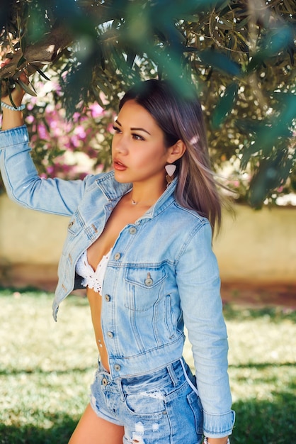 Beautiful blonde by the olive tree in denim jacket and shorts