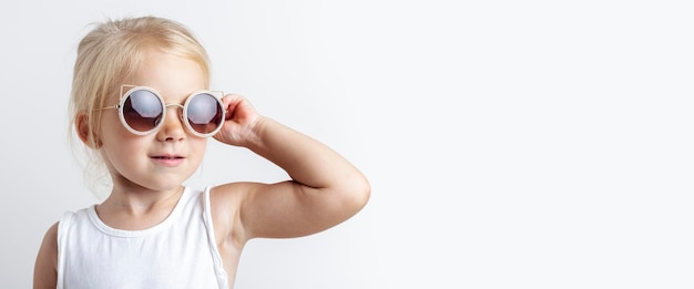 Beautiful blonde child in sunglasses on a light studio background. Banner.