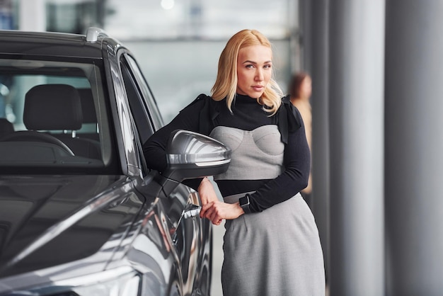 Beautiful blonde in elegant clothes standing near new modern car