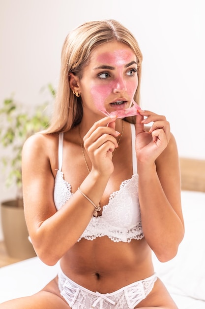 Beautiful blonde girl applies pink peeling mask on her face indoors