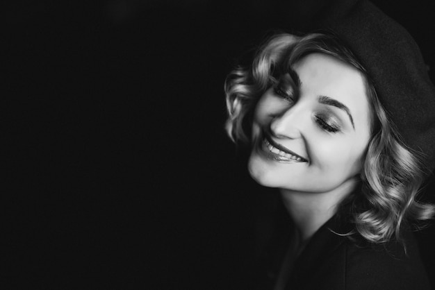 Beautiful blonde girl in a beret closed her eyes and smiles in retro style black and white