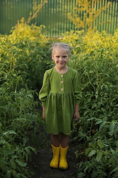 a beautiful blonde girl in a green dress and yellow boots is standing in the garden