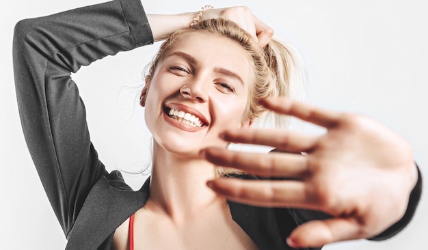 A beautiful blonde girl holds her hair and makes her own hairstyle with the emotion of happiness Woman pulls her hand towards the camera on a gray isolated background for advertising Nose piercing