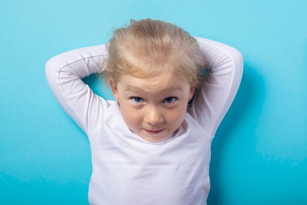 Photo beautiful blonde girl lying down holds her hands behind her head on a blue background. top view, flat lay.