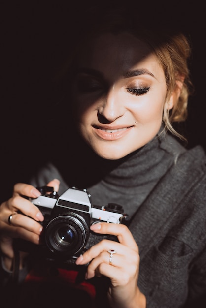 Beautiful blonde girl photographer in strict suit holds an old retro camerin her hands and smiles on sunny day. 