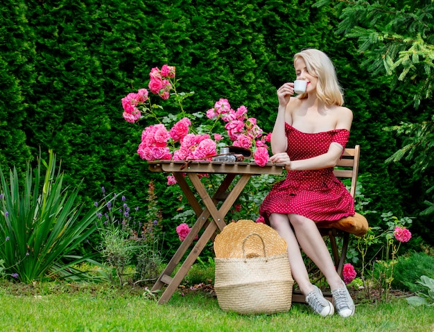 Beautiful blonde girl in red dress drinking a coffee in a garden