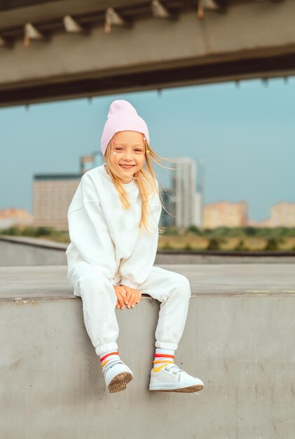 beautiful and blonde girl sits on a concrete fence against the backdrop of the cityscape copy space