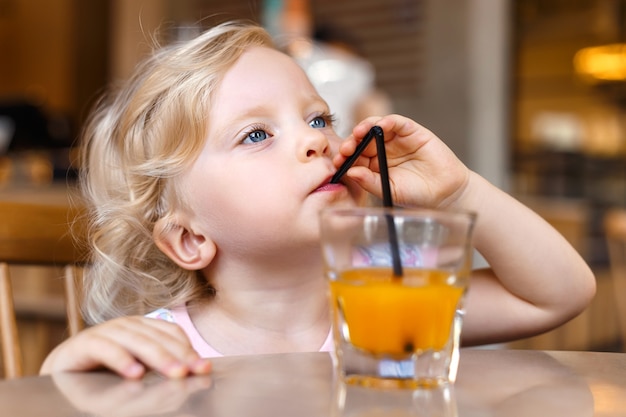 Beautiful blonde girl sitting at the table in the cafe outdoors drinking juice and eating desserts