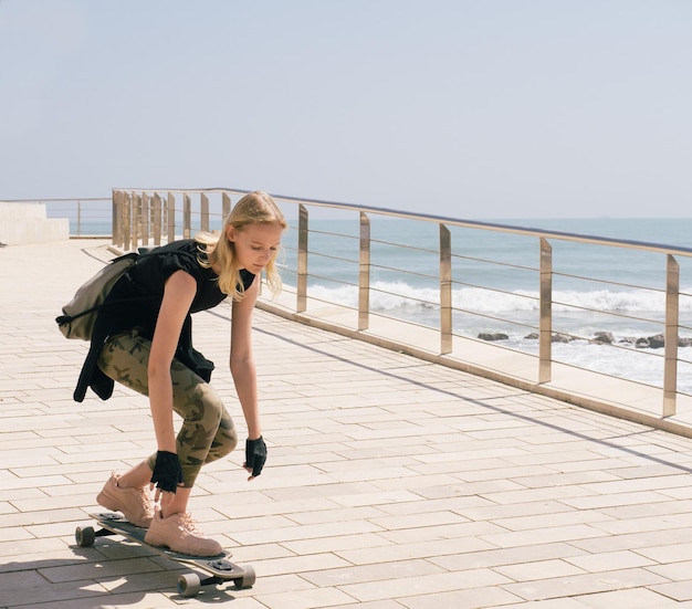 A beautiful blonde girl on skateboard in summer hot day on seafront