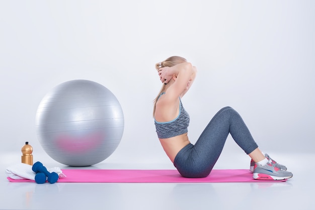 beautiful blonde girl in sportswear does exercises on a fitness Mat on a gray background