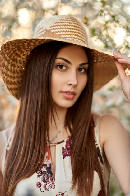 beautiful blonde girl with a bouquet of flowering branches in a straw hat and in a dress in a spring garden where trees bloom