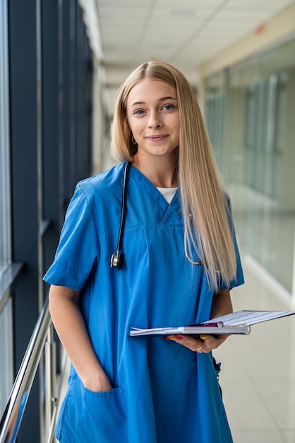 Photo beautiful blonde nurse holding a notebook with a pen in the hospital corridor. medicine concept