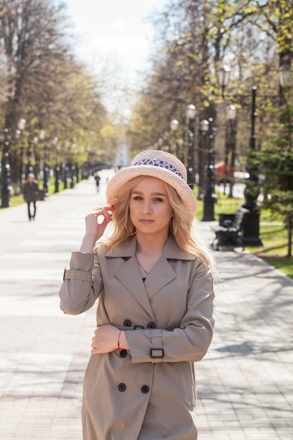 Beautiful blonde in a raincoat and hat on a walk in the park