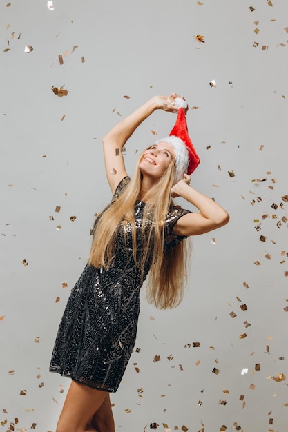 Beautiful blonde Santa girl dancing under glittering confetti New Year party concept