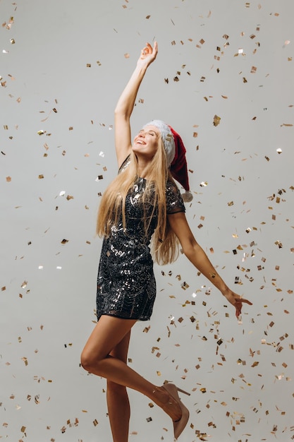 Beautiful blonde Santa girl dancing under glittering confetti New Year party concept