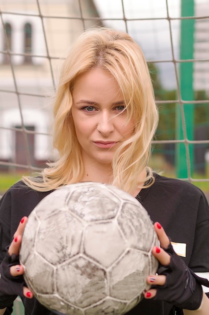 Beautiful blonde with a ball at the football goal