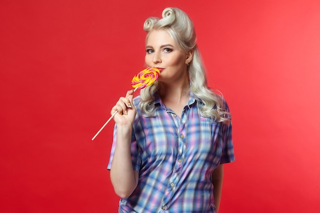 Beautiful blonde with a big candy, posing on a red background