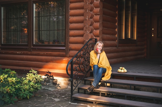 A beautiful blonde woman of about  years wrapped in a yellow blanket sits on the porch of a large wo...