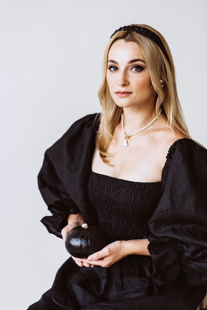 Beautiful blonde woman in a black linen dress with a pumpkin in her hands. Ethnic fashion, natural fabric. Halloween party. Soft selective focus.