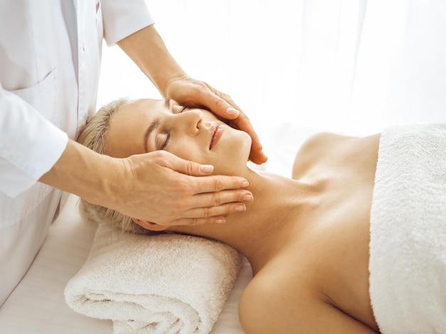 Beautiful blonde woman enjoying facial massage with closed eyes. Relaxing treatment in medicine and spa center concepts.