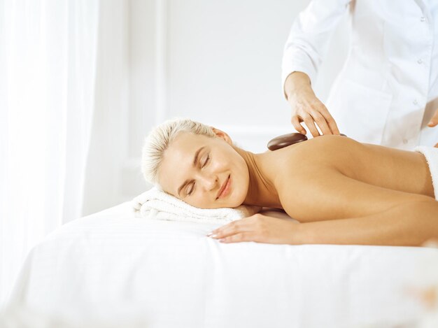 Beautiful blonde woman enjoying warm stones procedure with closed eyes. Spa concept.