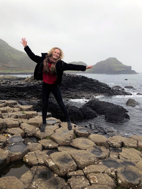 Beautiful blonde woman jumps above rocks of Giant's causeway Northern Ireland tourist attraction