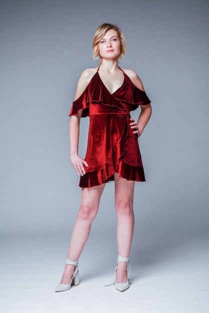 A beautiful blonde woman sits on a chair in a red dress in the studio