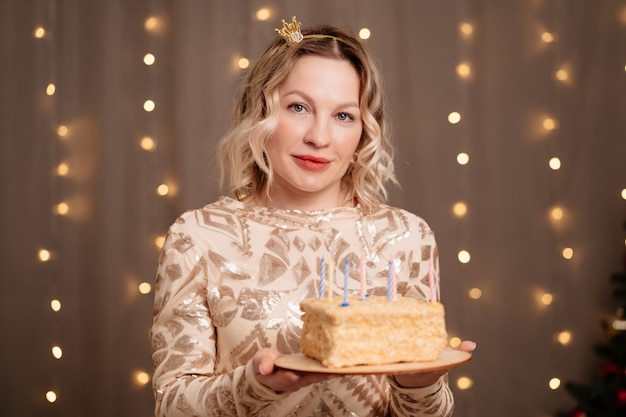 Beautiful blonde woman in a small crown on her head with a birthday cake and candles.