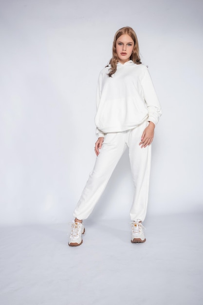 Beautiful blonde woman wear of white set of tracksuit isolated on gray background blonde girl in a white tracksuit stands on a white background