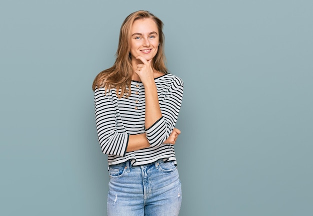 Beautiful blonde woman wearing casual clothes looking confident at the camera with smile with crossed arms and hand raised on chin thinking positive