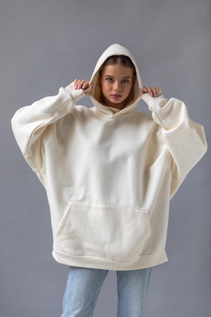 Beautiful blonde woman in a white hoodie and blue jeans posing on a gray background