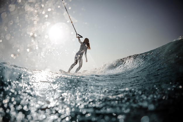 Beautiful blonde woman in the white swimsuit standing on the wakeboard holding a rope on the bending knees