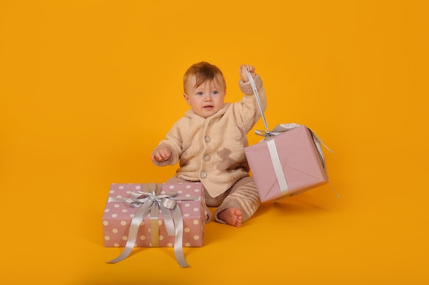 a beautiful blueeyed little boy in a knitted warm suit with gift boxes on a yellow background