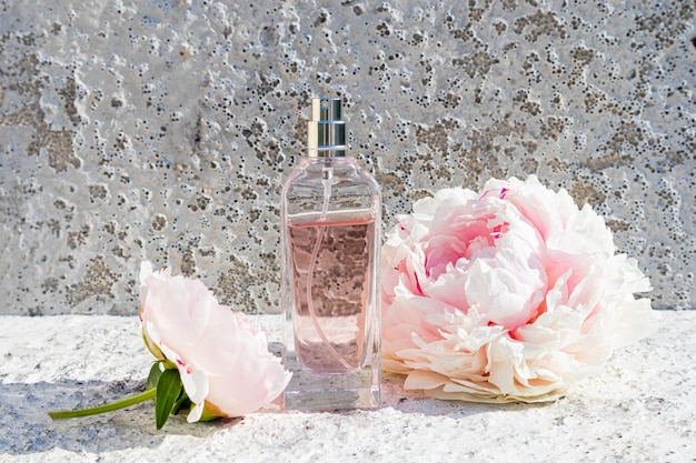 Beautiful bottle of women's perfume on a cement grey background with a chic flower of fragrant peony front view template for perfume