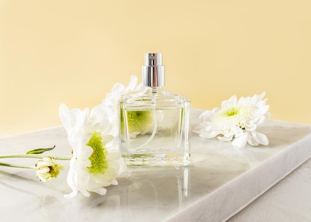 A beautiful bottle of women's perfume or spray stands on a white marble podium with white flowers front view An empty layout for your fragrance